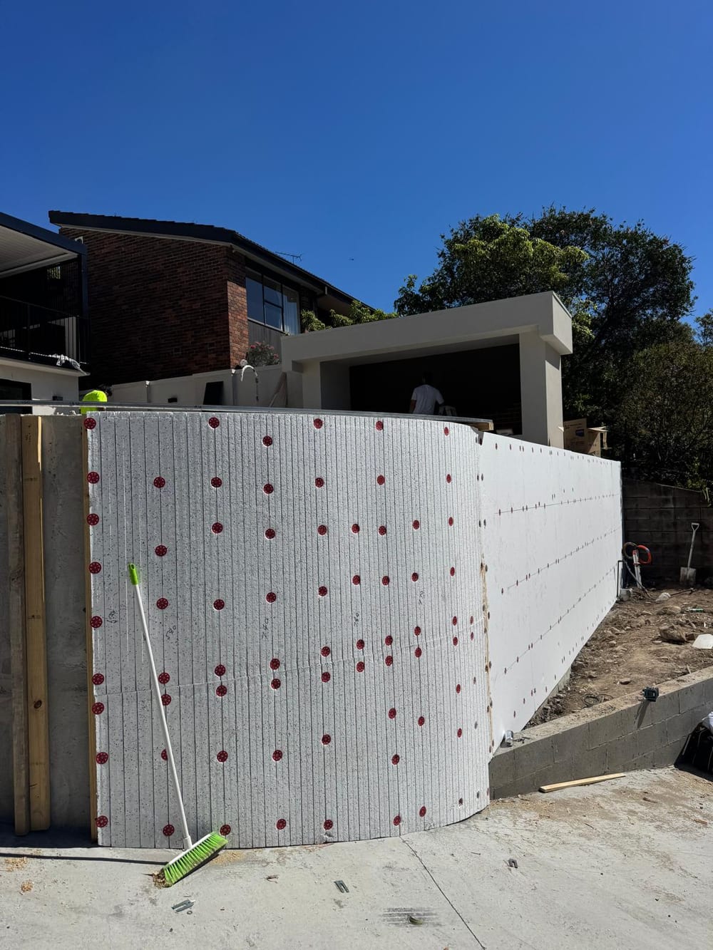 Curved raised pool wall clad in insulation board, beside a new cabana
