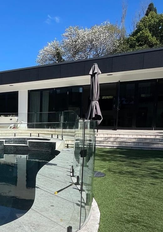 Finished Nabilton Group pool and spa set in a lawn behind frameless glass fencing, with the house and garden beyond