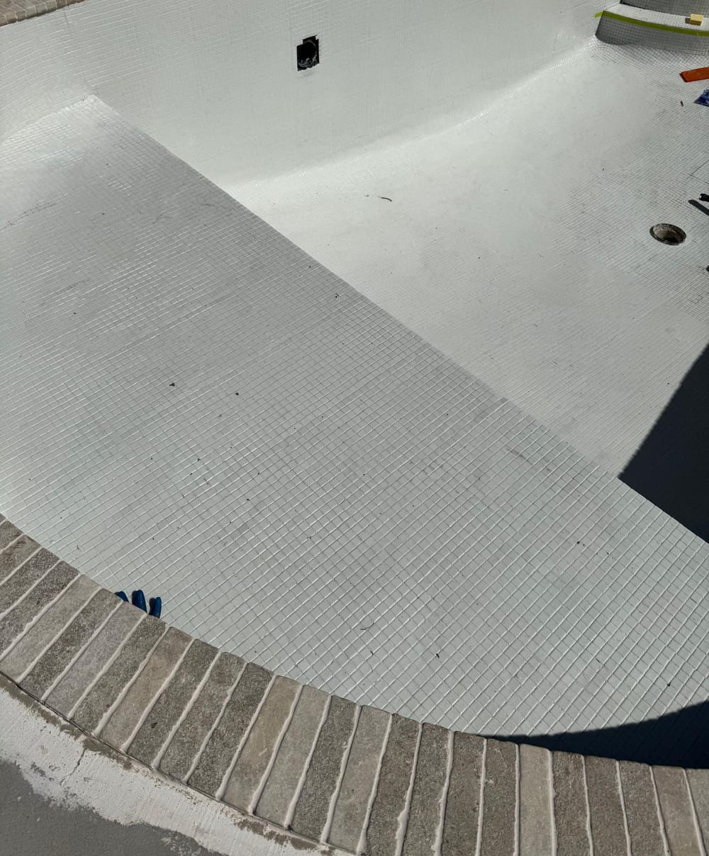 White mosaic tiling laid through the floor and benches of a pool shell