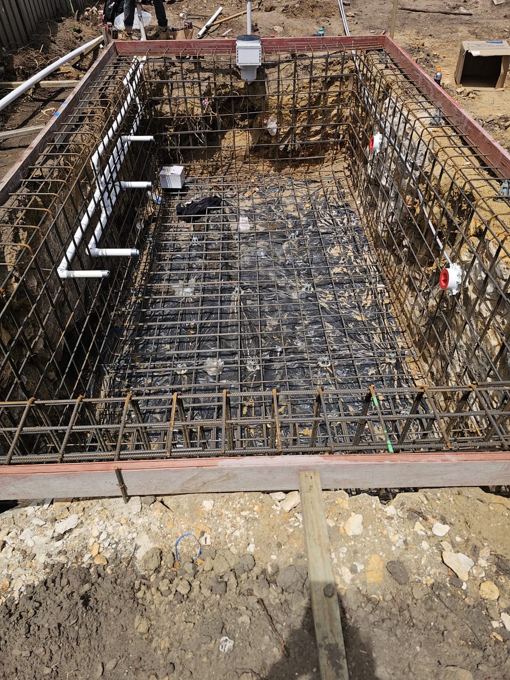 Steel reinforcement cage and wall plumbing in a rectangular pool excavation