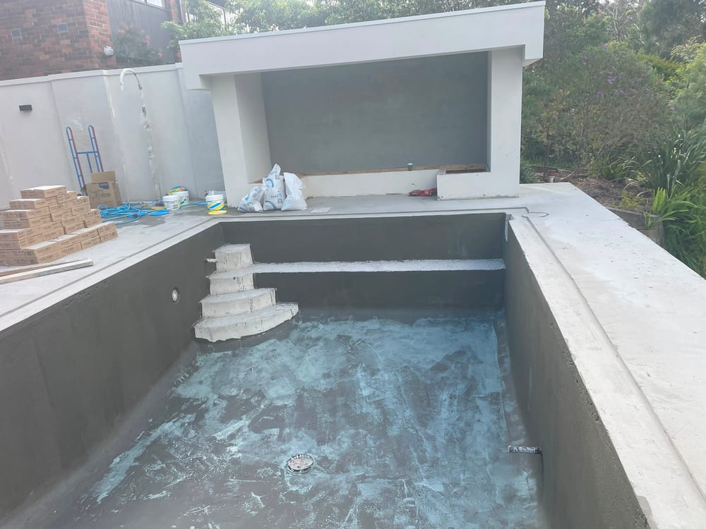 Waterproofed concrete pool shell with entry steps and a bench seat, beside a rendered cabana